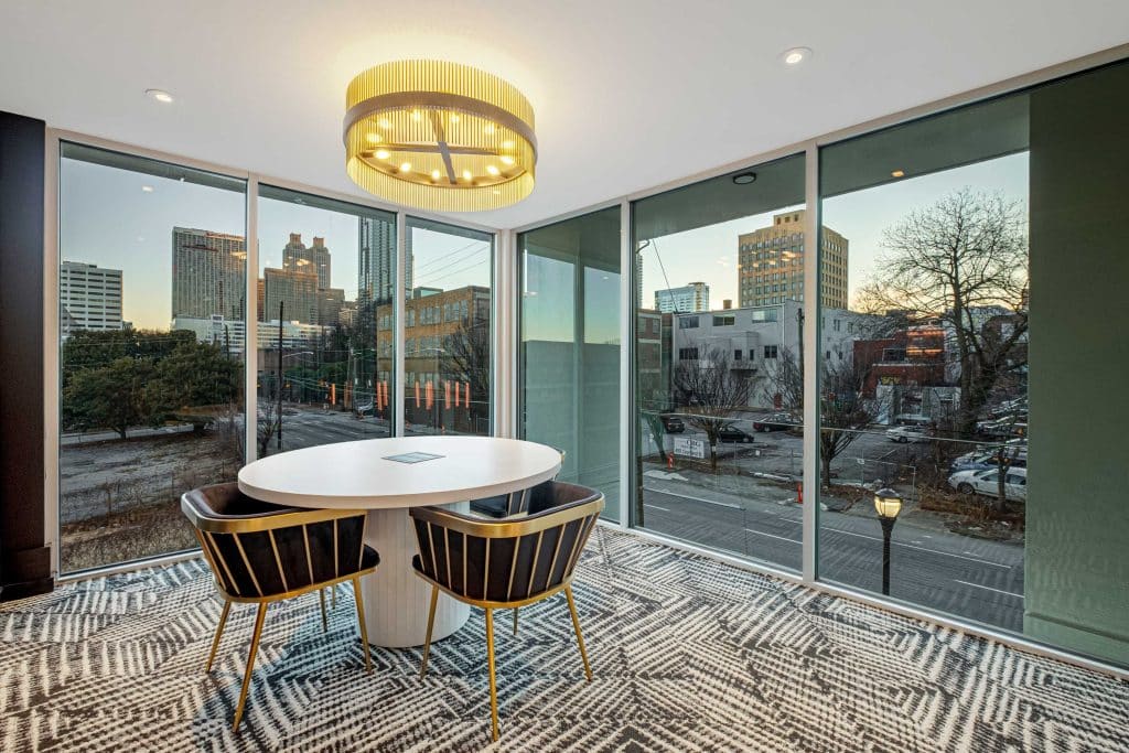 Furnished office space with desk and chairs with floor to ceiling windows at dusk